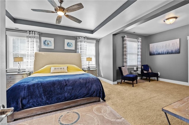 bedroom featuring multiple windows, carpet flooring, a raised ceiling, and baseboards