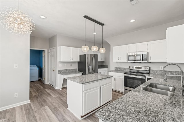 kitchen featuring washer / clothes dryer, appliances with stainless steel finishes, a sink, a kitchen island, and light stone countertops