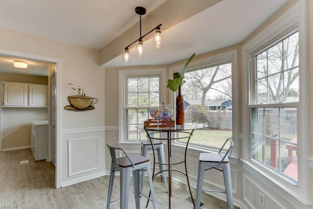 dining area with light wood finished floors, a decorative wall, separate washer and dryer, and wainscoting