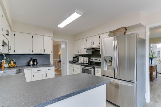 kitchen featuring appliances with stainless steel finishes, dark countertops, a sink, and decorative backsplash