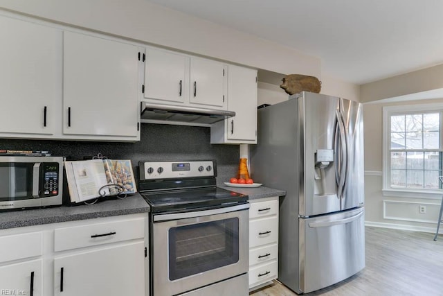 kitchen featuring under cabinet range hood, white cabinetry, appliances with stainless steel finishes, light wood-type flooring, and dark countertops