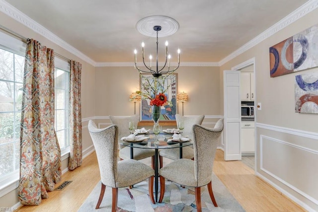 dining area with light wood finished floors, visible vents, ornamental molding, and a notable chandelier