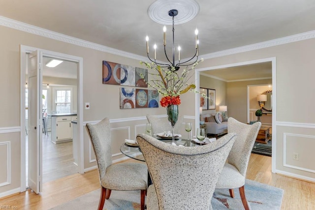 dining room with light wood-style floors, a notable chandelier, a decorative wall, and crown molding