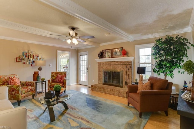 living room with a textured ceiling, a fireplace, light wood-style floors, ornamental molding, and beam ceiling