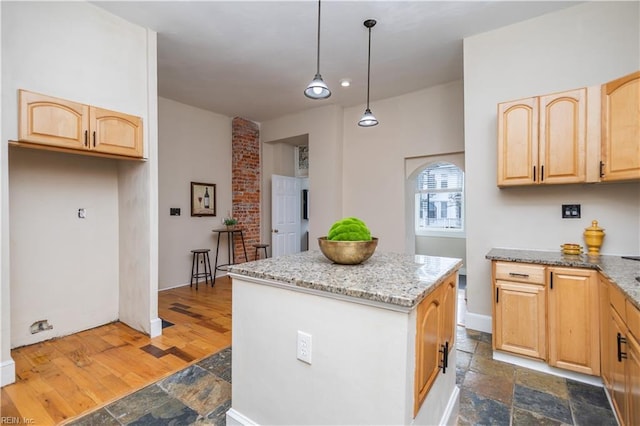 kitchen with light stone countertops, stone tile floors, a kitchen island, and light brown cabinetry