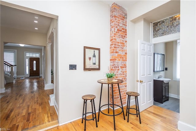 corridor with decorative columns, a healthy amount of sunlight, a sink, wood finished floors, and baseboards