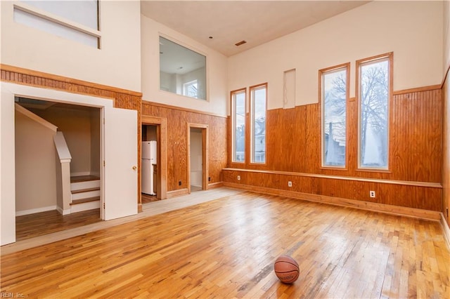 unfurnished living room with a high ceiling, wainscoting, wooden walls, hardwood / wood-style floors, and stairs