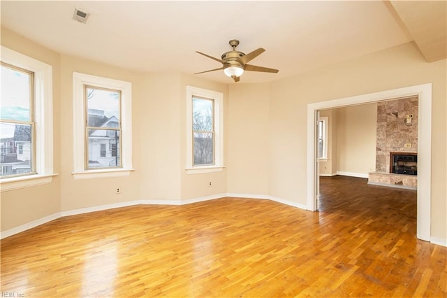 empty room with a large fireplace, plenty of natural light, wood finished floors, and baseboards