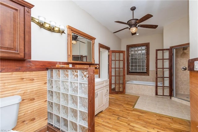 full bath with a ceiling fan, tiled shower, toilet, wood finished floors, and a garden tub