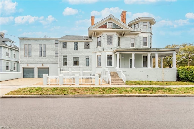 view of front facade with concrete driveway, a chimney, an attached garage, covered porch, and fence