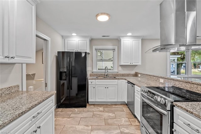 kitchen with light stone counters, appliances with stainless steel finishes, white cabinets, a sink, and wall chimney range hood