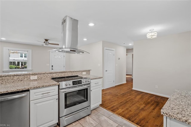 kitchen featuring light stone counters, recessed lighting, island range hood, stainless steel appliances, and white cabinets