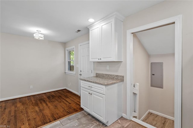 kitchen featuring electric panel, baseboards, visible vents, light stone counters, and white cabinetry