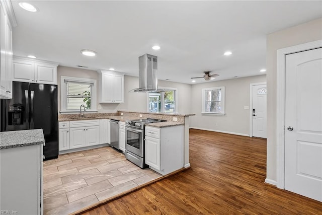 kitchen featuring island range hood, light wood-style flooring, a peninsula, stainless steel appliances, and a sink