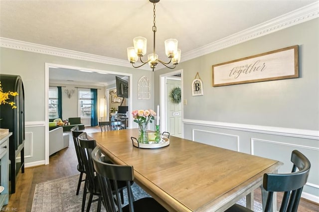 dining room with crown molding, dark wood-type flooring, a wainscoted wall, and an inviting chandelier