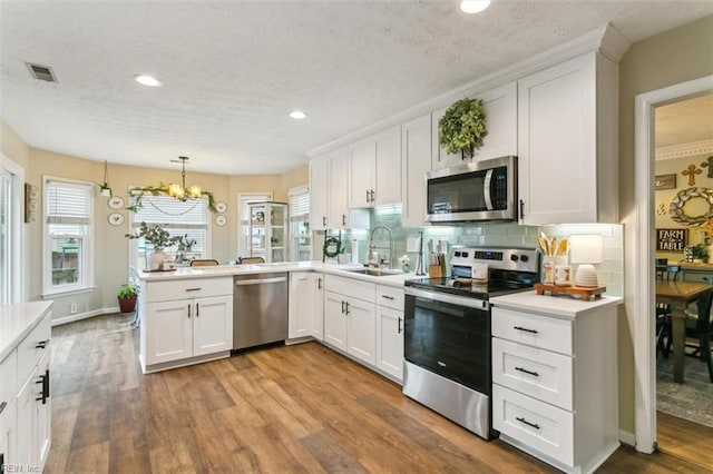 kitchen featuring a peninsula, a sink, visible vents, appliances with stainless steel finishes, and light wood-type flooring