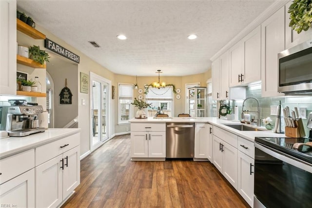 kitchen with white cabinets, dark wood-style floors, appliances with stainless steel finishes, a peninsula, and a sink