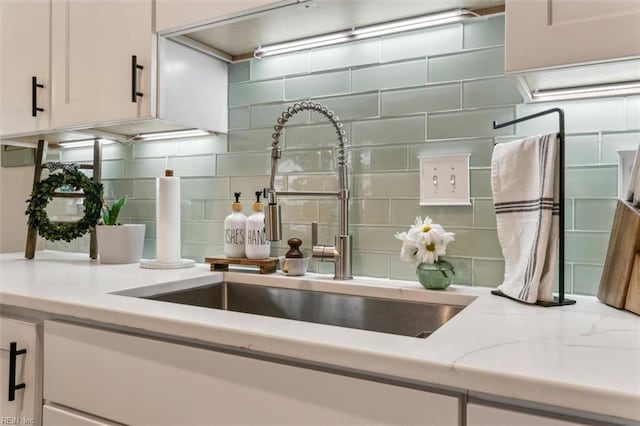 kitchen featuring light stone countertops, tasteful backsplash, white cabinets, and a sink