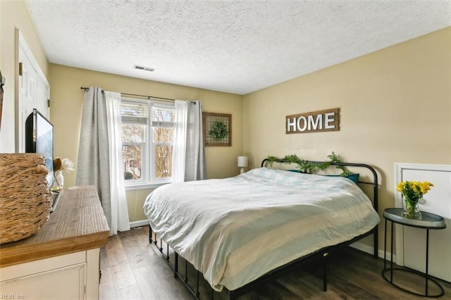 bedroom featuring baseboards, a textured ceiling, visible vents, and wood finished floors