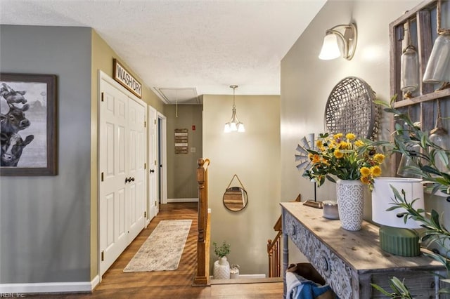 corridor featuring attic access, a textured ceiling, an upstairs landing, wood finished floors, and baseboards