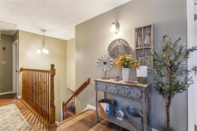 hall with attic access, a textured ceiling, an upstairs landing, and wood finished floors