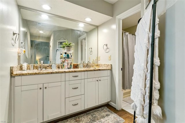 full bathroom featuring double vanity, wood finished floors, a stall shower, and a sink