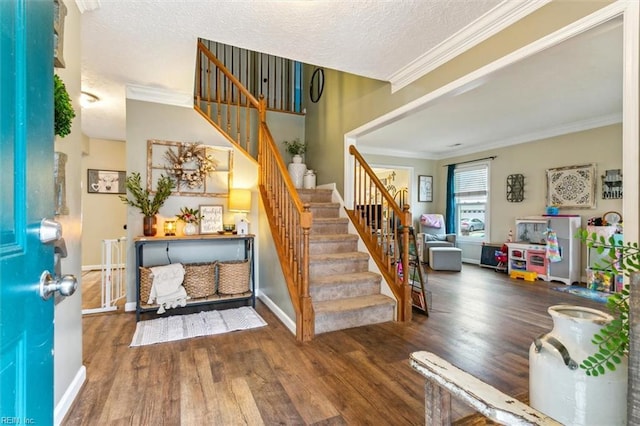 foyer entrance featuring a textured ceiling, wood finished floors, baseboards, stairs, and ornamental molding