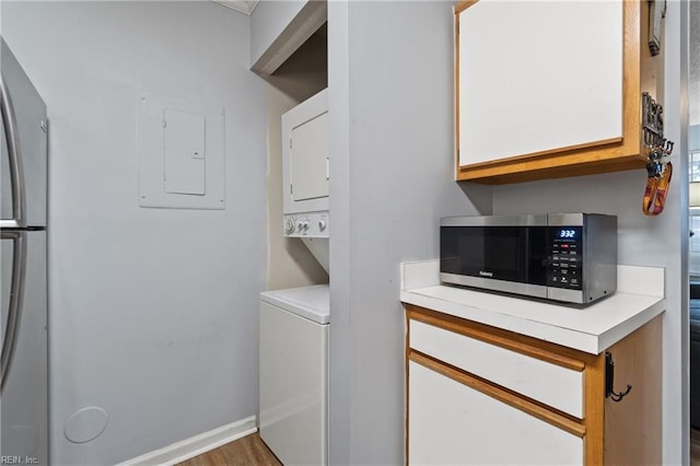 laundry room with wood finished floors, stacked washer and clothes dryer, electric panel, and laundry area