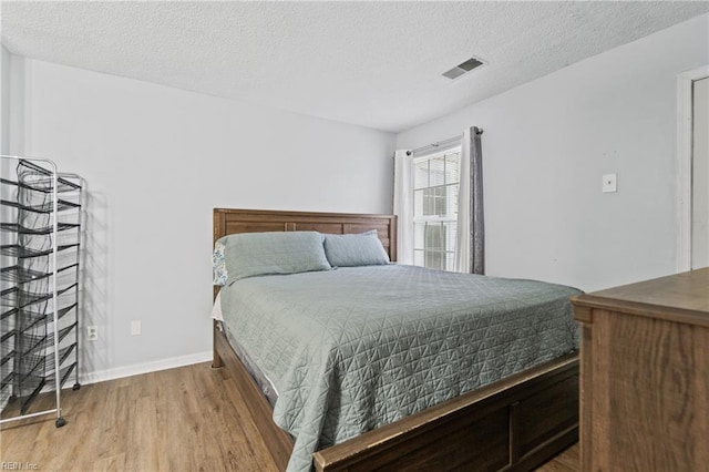 bedroom featuring visible vents, a textured ceiling, baseboards, and wood finished floors