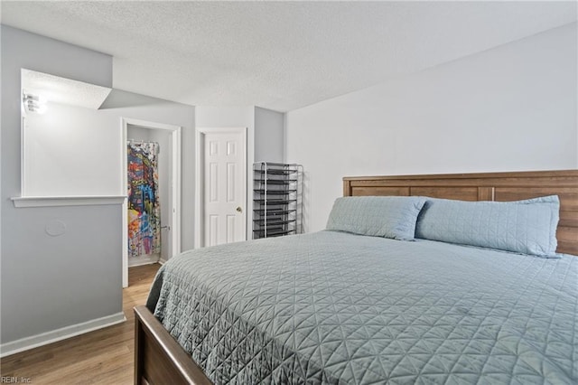 bedroom featuring a closet, a textured ceiling, baseboards, and wood finished floors