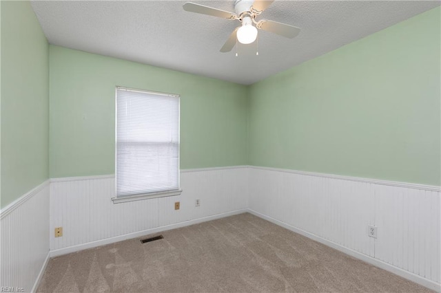 carpeted spare room with a wainscoted wall, ceiling fan, visible vents, and a textured ceiling