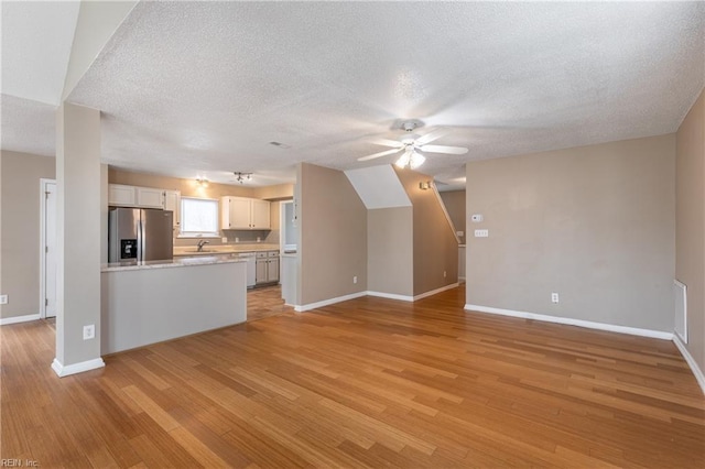 unfurnished living room with light wood-style floors, a textured ceiling, baseboards, and a ceiling fan