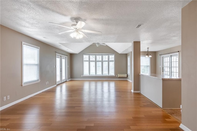 unfurnished room featuring visible vents, vaulted ceiling, wood finished floors, baseboards, and ceiling fan with notable chandelier