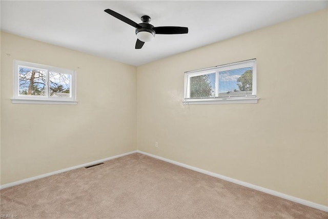 carpeted spare room with visible vents, baseboards, and a ceiling fan