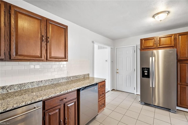 kitchen featuring brown cabinets, backsplash, stainless steel appliances, light tile patterned floors, and light stone countertops