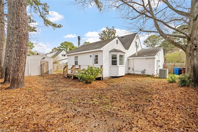 rear view of property featuring a shed, central air condition unit, an outdoor structure, and fence