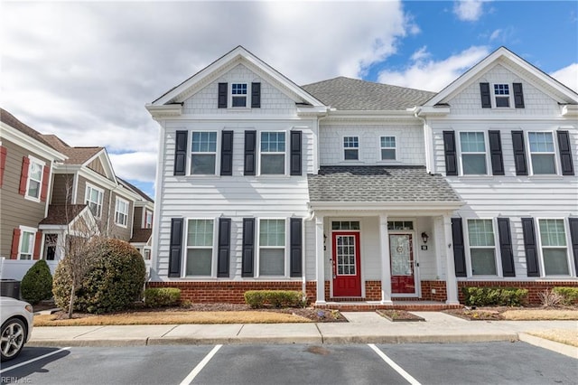 townhome / multi-family property featuring uncovered parking, brick siding, and roof with shingles