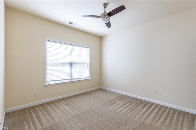 empty room featuring a ceiling fan, light colored carpet, visible vents, and baseboards