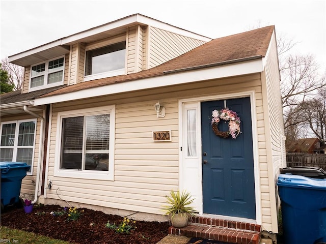 view of exterior entry with a shingled roof and fence