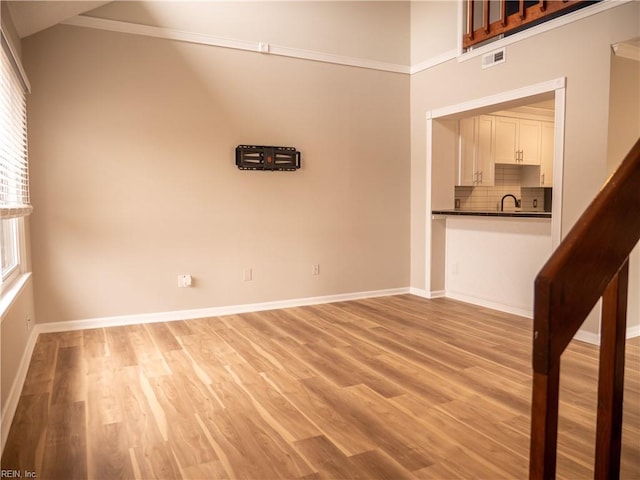 unfurnished room featuring vaulted ceiling, light wood finished floors, visible vents, and baseboards