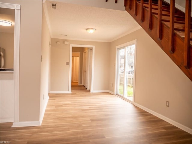 interior space featuring a textured ceiling, light wood-style flooring, visible vents, baseboards, and ornamental molding