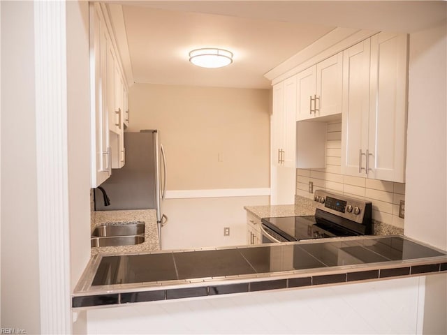 kitchen with appliances with stainless steel finishes, backsplash, a peninsula, white cabinetry, and a sink