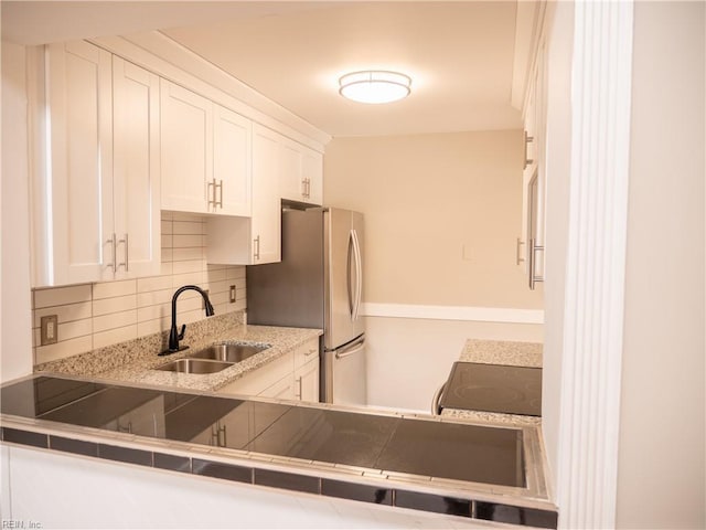 kitchen with electric range oven, decorative backsplash, freestanding refrigerator, white cabinets, and a sink