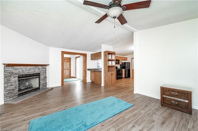 living area with light wood finished floors, lofted ceiling, a stone fireplace, a textured ceiling, and baseboards