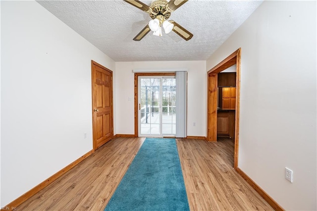 doorway to outside with a textured ceiling, light wood-type flooring, a ceiling fan, and baseboards