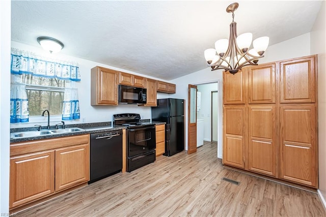 kitchen featuring dark countertops, decorative light fixtures, light wood-type flooring, black appliances, and a sink