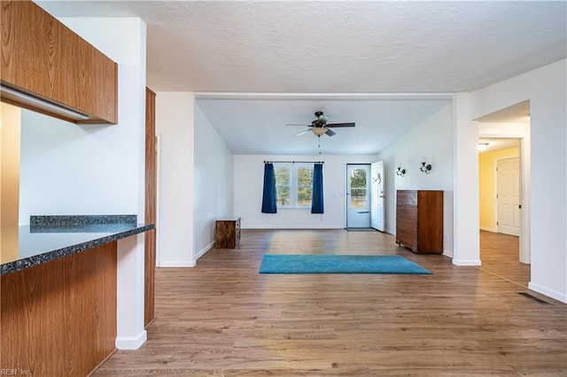 doorway featuring a ceiling fan, baseboards, a textured ceiling, and light wood finished floors