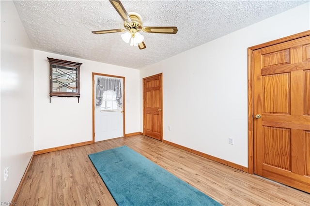 interior space featuring a textured ceiling, baseboards, a ceiling fan, and light wood-style floors