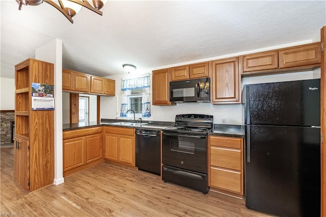 kitchen with light wood finished floors, brown cabinetry, dark countertops, black appliances, and a sink