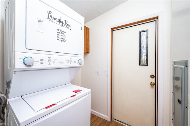 washroom featuring laundry area, light wood finished floors, baseboards, stacked washer / dryer, and a textured ceiling